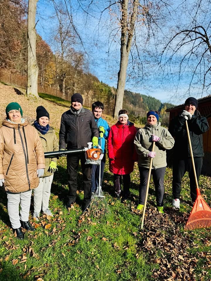 Uczestnicy z grabiami i dmuchawą podczas jesiennego grabienia liści przy ośrodku